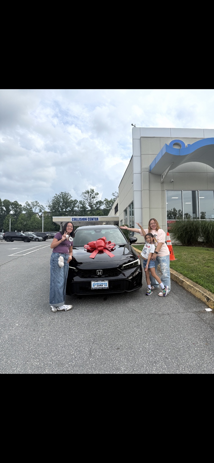 Family celebrating beside a black Honda with a red bow