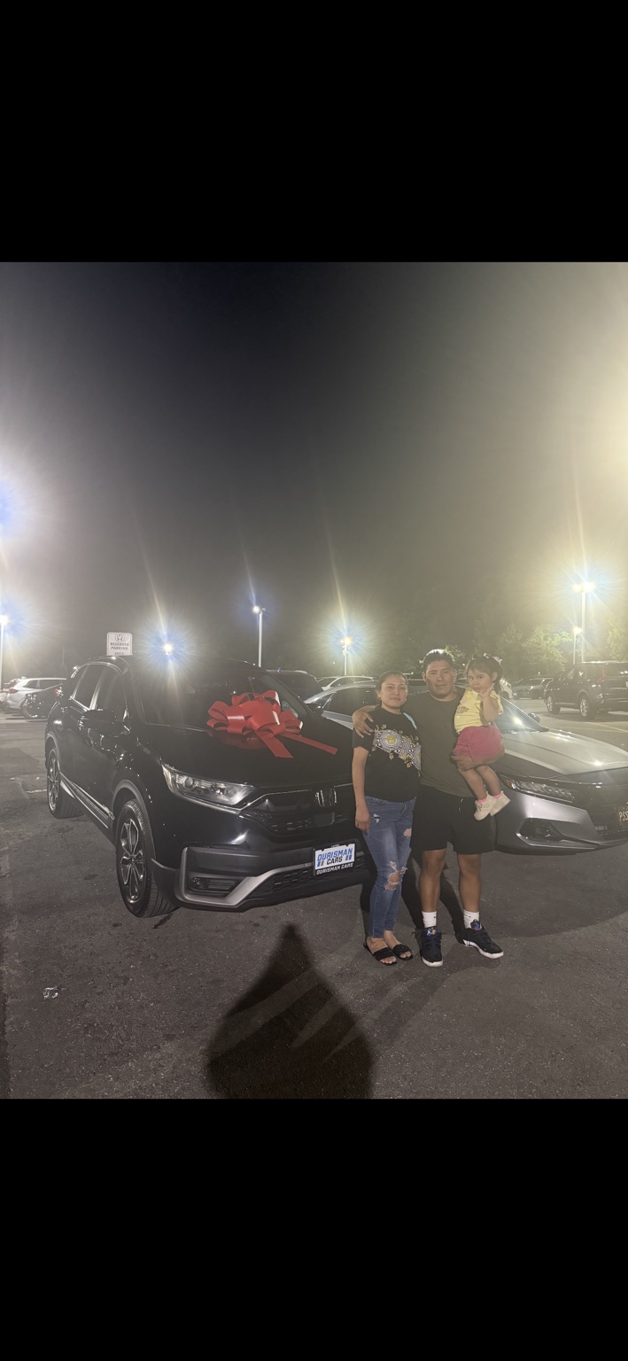 Family beside a dark Honda SUV with a red bow at night