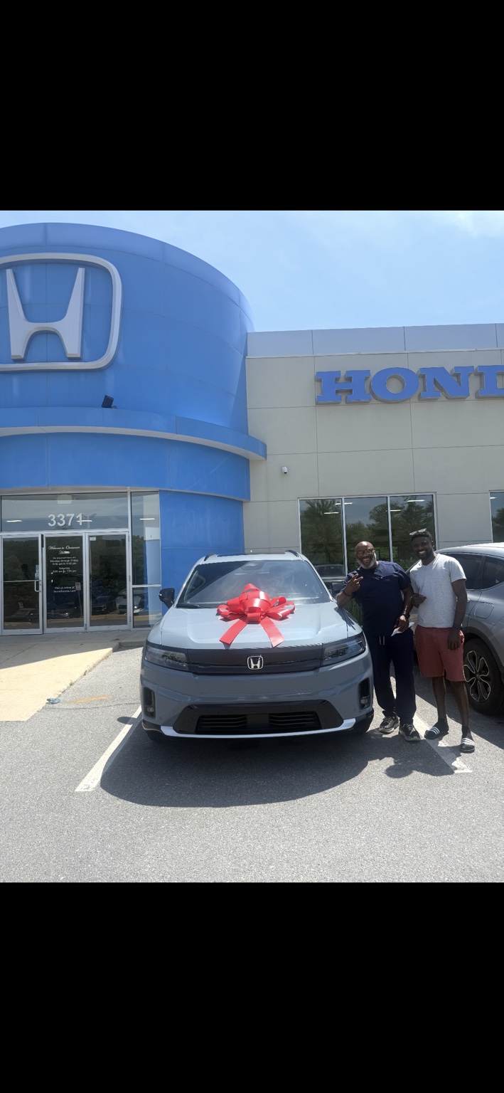 Two customers beside a blue-gray Honda SUV with a red bow
