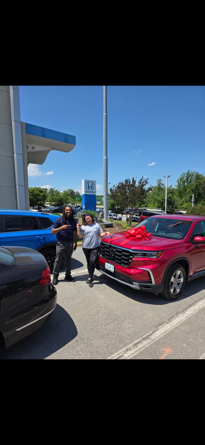 Two people celebrating beside a red Honda SUV with a bow