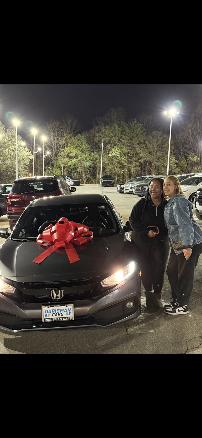 Two customers beside a gray Honda sedan with a red bow at night