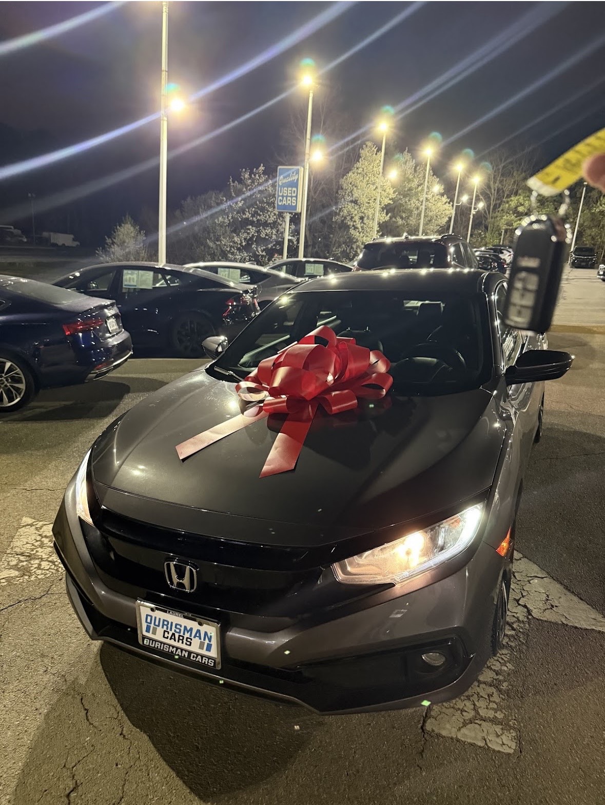 Honda delivery with a red bow and keys held up on the car lot at night